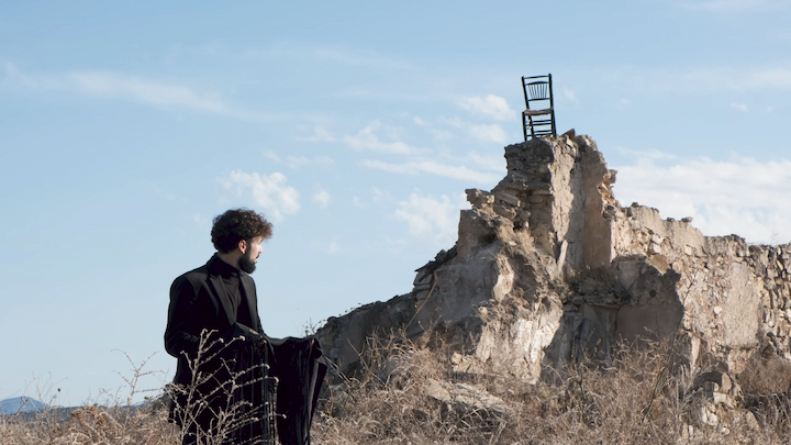 The singer looking at a chair on top of a ruined house